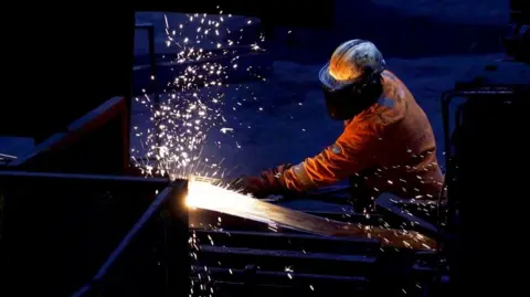 PA Media A steelworker in full protective gear working at a steel plant. Sparks are flying as he appears to cut through a material