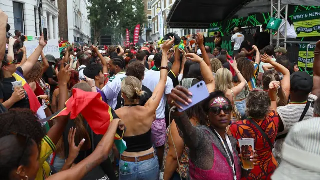 A group of people dancing in front of a stage that is branded with Wray and Nephew's logo.