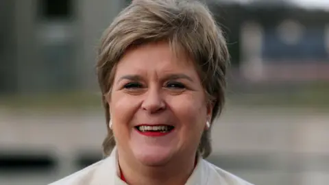 Getty Images Nicola Sturgeon smiling at the camera, wearing a white coat and red lipstick