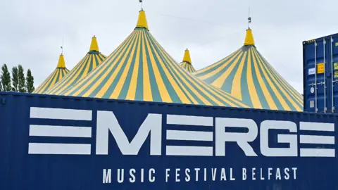 Pacemaker A green and yellow tent behind a shipping container with Emerge printed on the side of it 