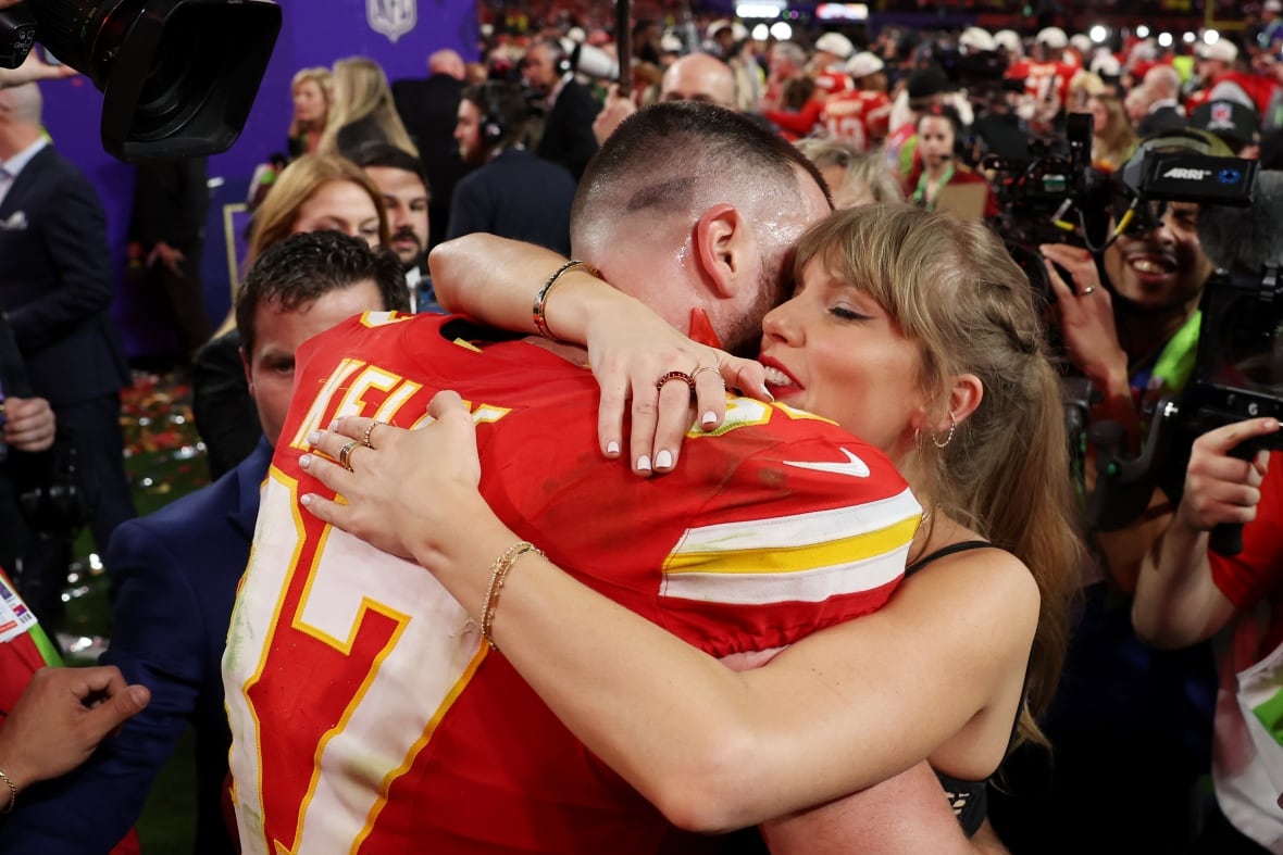 A male football player without his helmet on hugs a woman as media members take pictures.