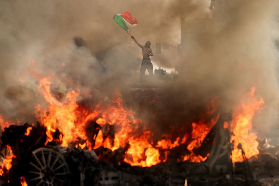 A man waves a Mexican flag as smoke and flames rise from a burning vehicle during a protest against federal immigration sweeps in downtown Los Angeles on June 8.