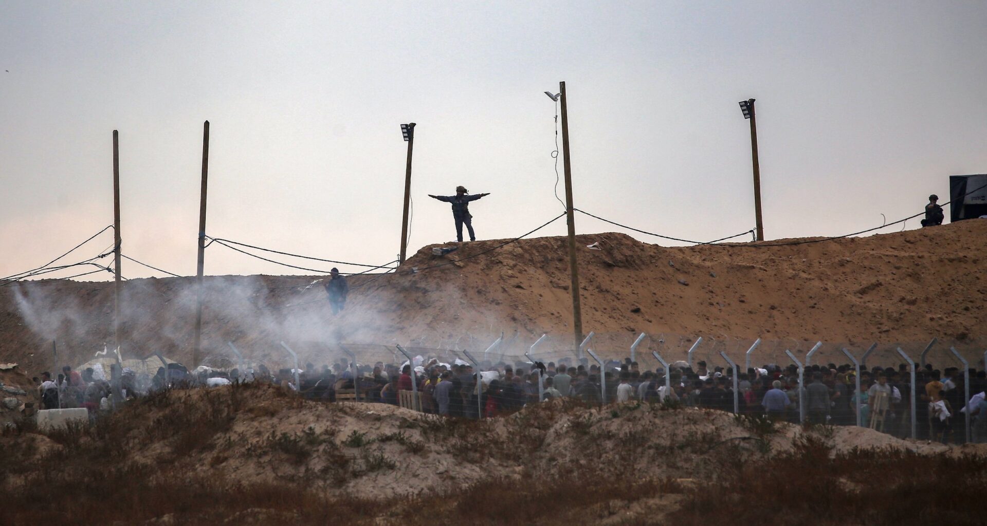 Members of a private U.S. security company, contracted by the Gaza Humanitarian Foundation (GHF), direct displaced Palestinians as they gather to receive relief supplies at a distribution centre in the central Gaza Strip on June 8, 2025, as smoke bombs are fired by Israeli troops.