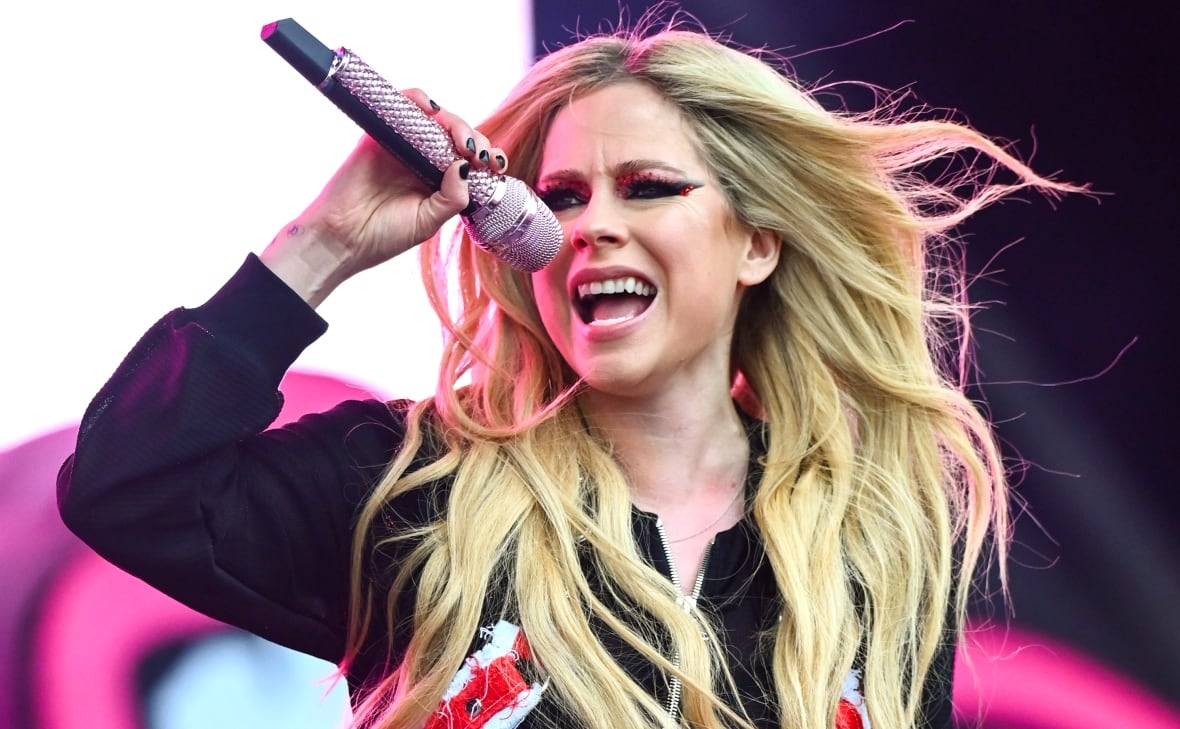 Avril performs holding a sparkly mic while wearing black eyeliner and a black hoodie.