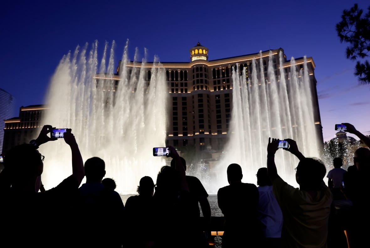 Visitors in silhouette watch and take cellphone stills of a Fountains of Bellagio water show, at night.