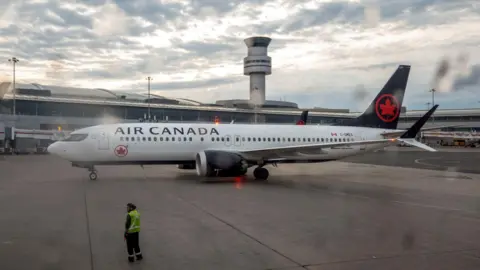 Reuters An Air Canada aircraft sits on a runway with an air traffic control tower in the background.