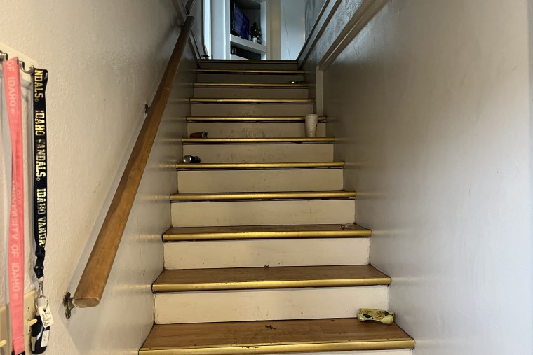Shot of the stairs. 4 empty cans and a takeout drink are on the stairs. 2 lanyards are hanging on the rack, pink and black univerity of Idaho.