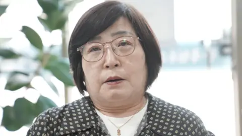 BBC/Hyojung Kim A middle-aged woman with short black hair and glasses looks into the camera