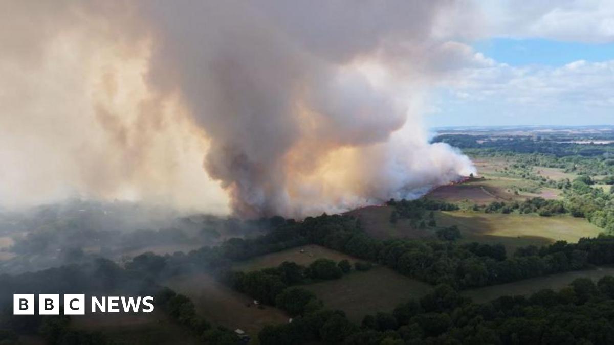 White smoke flowing up into the sky seen from above a large fire on a heath.