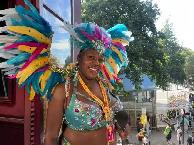 A woman smiles wearing blue multicoloured wings and a jewelled outfit