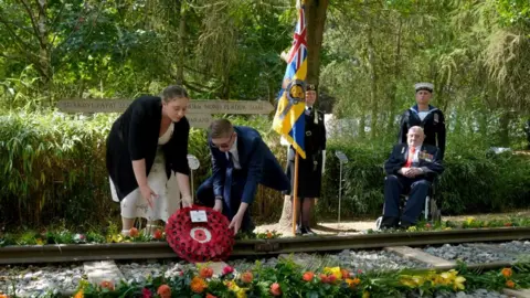 PA Media Second World War veteran Alfred Conway (right) from Lincolnshire, who served with the Royal Navy, watches on as his great-grandchildren, Sarah-Jayne Carpenter (left) and James Carpenter (second left) lay a wreath on the Burma Thailand Railway memorial at the National Memorial Arboretum