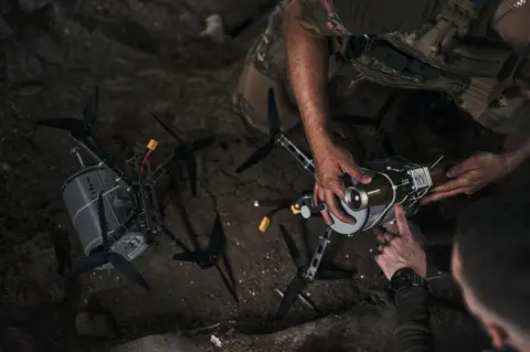 Getty Images An arm holds on to a silver-coloured drone perched on the ground in the dark
