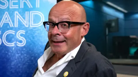 BBC Harry Hill in the Desert Island Discs studio, wearing a suit with an open-collar shirt