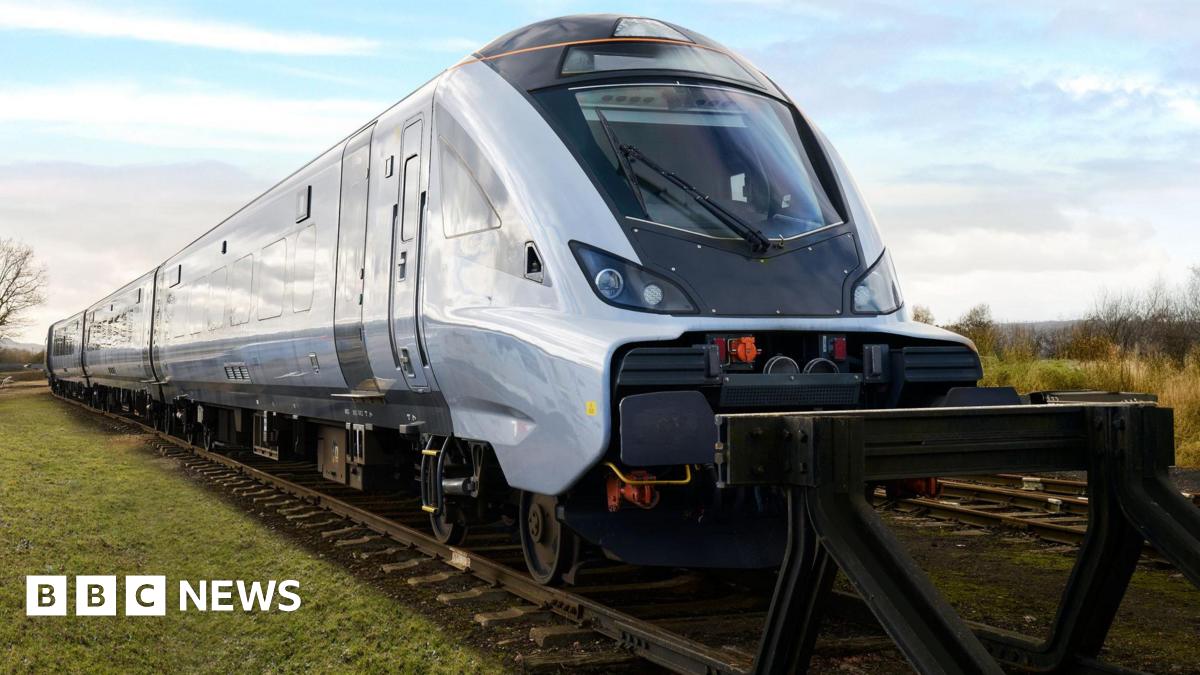 A large silver train stopped at the end of a railway line in a green field.