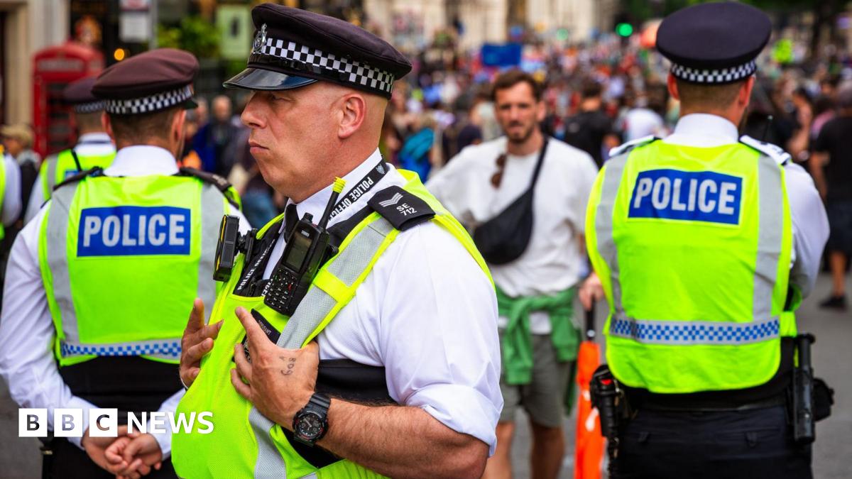 Three police officers stand in high visibility vests in a crowd of people as one man dressed in summer clothes approaches them