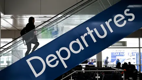 Getty Images Silhouette of a woman travelling from the ground to the first floor on an escalator at Glasgow Airport. A blue and white sign reading "Departures" can be seen on the side of the escalator.
