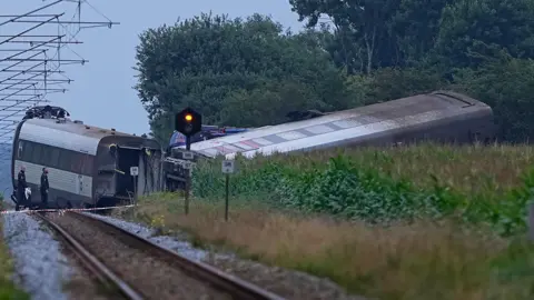 AFP Two police look at a train carriage, which is on its side and at an angle from the engine