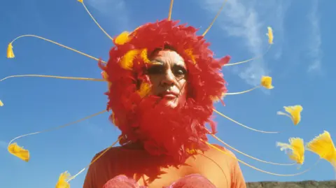 Alamy Stamp is wearing a flamboyant red head dress in The Adventures of Priscilla, Queen of the Desert in 1994