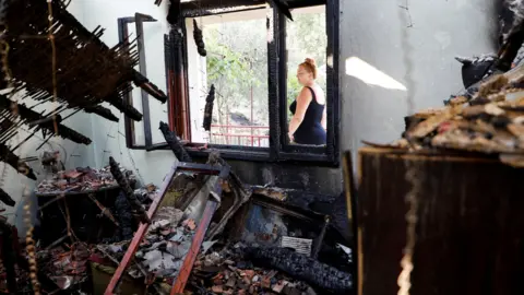 Reuters A woman in a black sleevless dress looks passes by the burnt out shell of her home in Piperi Village, Montenegro.