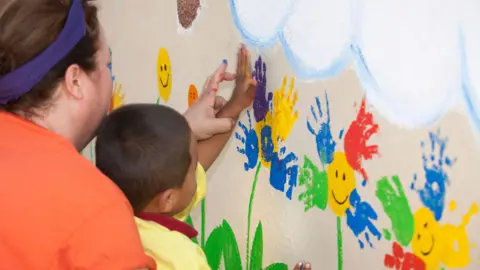 Getty Images Woman helps young child hand paint on a wall 