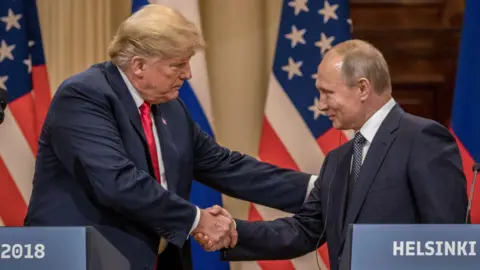 Getty Images Trump and Putin shaking hands in front of a lectern reading "Helsinki". American and Russian flags are in the background