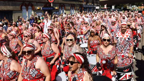 Reuters A group of performers in red, black and white patterned clothing, banging drums during the parade. 