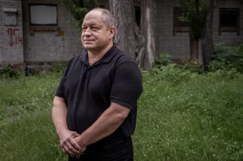 Dr Serhii Andriichenko stands in a grassy area, wearing a black polo shirt, his hands clasped in front of him.