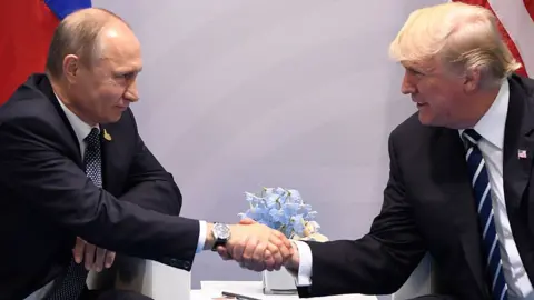 AFP via Getty Images Vladimir Putin and Donald Trump shake hands across a table at the G20 summit in Hamburg, Germany, in July 2017 as they look at each other directly. 