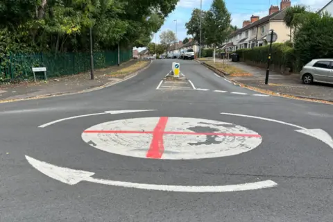 A red cross of St George spray painted onto a mini white roundabout on a residential street.