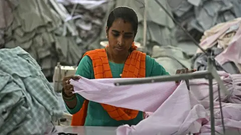 AFP via Getty Images A garment worker wearing a green dress and saffron scarf sorts tailored shirts at an apparel manufacturing unit in Bengaluru on August 25, 2025.
