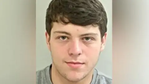 Police handout Custody image of Henry Houghton: a young man with brown hair, wearing a grey t-shirt.