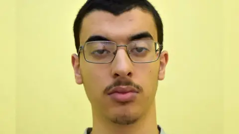 Greater Manchester Police A headshot of Hashem Abedi wearing glasses facing the camera against a yellow background. 