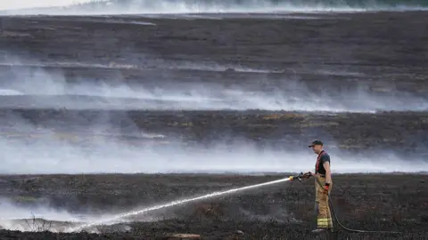 Getty Images A firefighter using a water cannon to dampen down moorland on Langdale Moor.