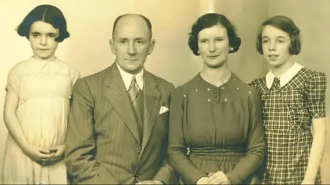 Dame Stephanie Shirley In a black and white photograph a young Dame Stephanie is pictured to the left of her parents and sister wearing a pale dress while her family also pose with neutral expressions in smart clothes