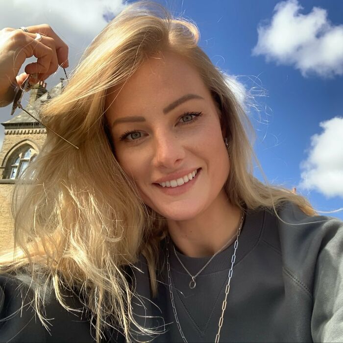 Smiling woman with blonde hair outside on a sunny day, representing woman’s 15,500-ft jump after breakup story.