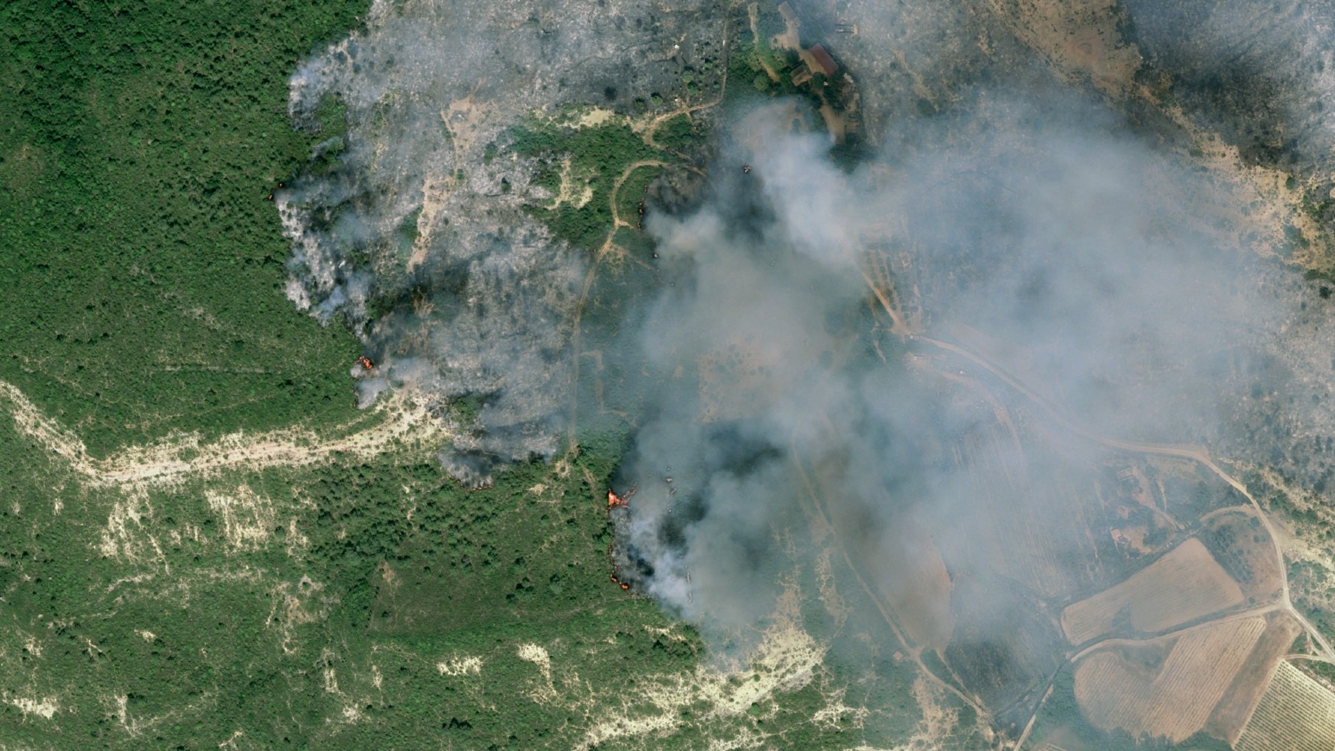 fire and smoke rolls through a green countryside as seen from space
