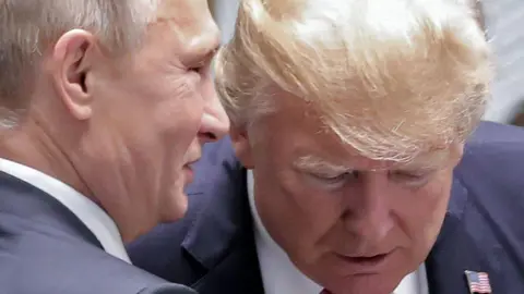 Getty Images Vladimir Putin appears to speak directly into the ear of Donald Trump in a close-up from a summit in Vietnam in November 2017. Trump, wearing a US flag pin on his lapel, is looking down and is seen from the front, while Putin is in profile. 