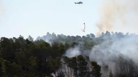Reuters A helicopter battles a wildfire while firefighters work on ground, near Saint-Laurent-de-la-Cabrerisse