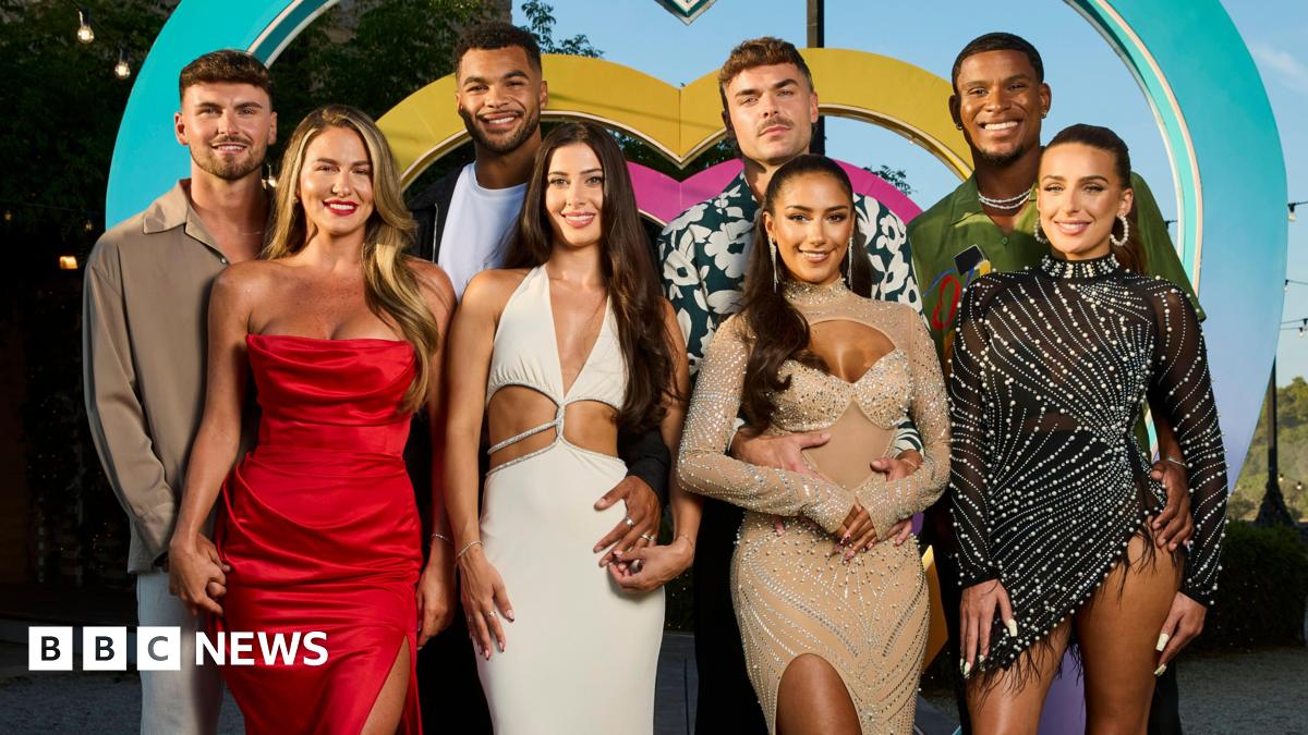 The eight Love Island finalists stood smiling in front of a blue, pink and yellow heart.