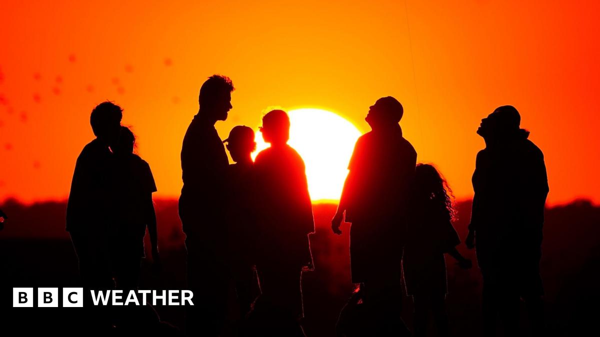 A group of people silhouetted against a background of an orange sky and a setting Sun