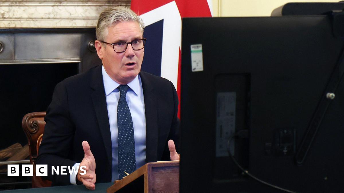 Keir Starmer sitting at a desk in front of a fireplace and a union flag. In the foreground is the back of a computer.