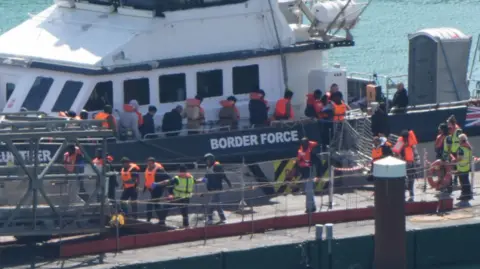 PA Media A group of migrants wearing life jackets being led off a Border Force vessel at the Port of Dover on Saturday