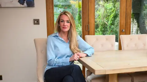 Orla Minihane sits on a beige dining chair at her home 
