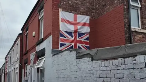 Adikia Media Union flag and St George's flag on the side of a terraced house