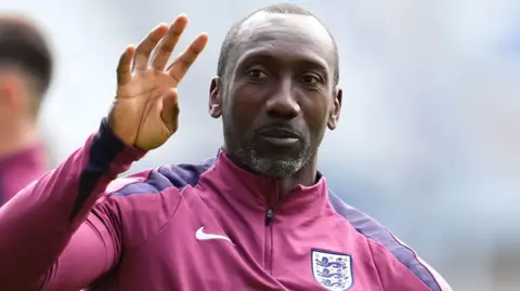 PA Media Jimmy Floyd Hasselbaink with an England training top and one hand raised