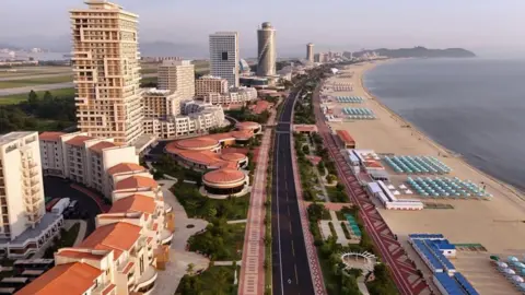 KCNA A Korean Central News Agency photo showing an aerial view of the Wonsan Kalma Coastal Tourist Zone, with dozens of buildings, an empty road and many beach umbrellas on the beachfront