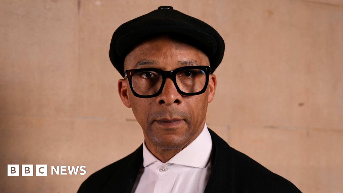 Jay Blades wearing a black cap, black jacket and white shirt