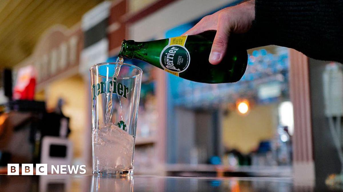 Mags Haney outside her home in the Raploch talking to two police officers. The photo from the mid 1990s shows Haney with short bleached blond hair and big earrings. She is wearing a pink cardigan and and orange t-shirt. A number of locals are standing around watching the scene
