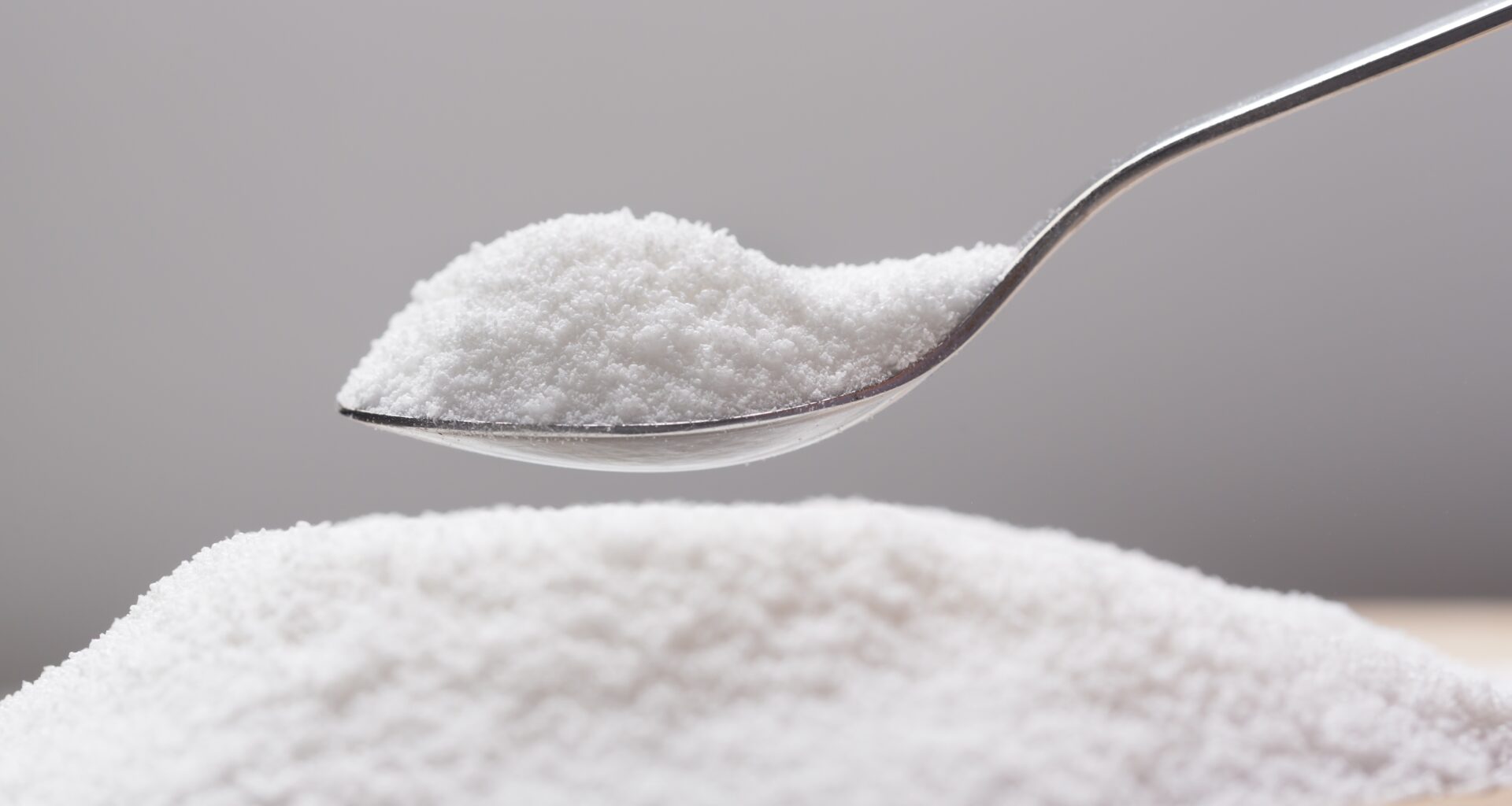 pile of flaky white sweetener on a spoon, above a larger pile of the sweetener