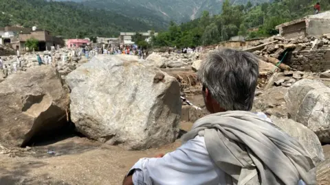 BBC A grey-haired man from behind, looking at large boulders in the foreground and other debris in the background
